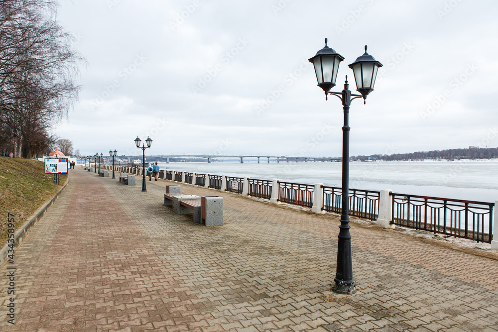 Riverwalk along frozen Volga River in the city of Kostroma in early spring. Paved embankment, benches and lanterns under grey cloudy skies. Kostroma, Popular travel destination of Golden Ring,  Russia