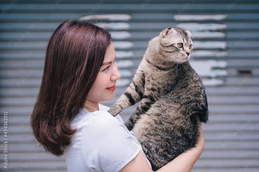 A young woman was holding a cat in front of the house.