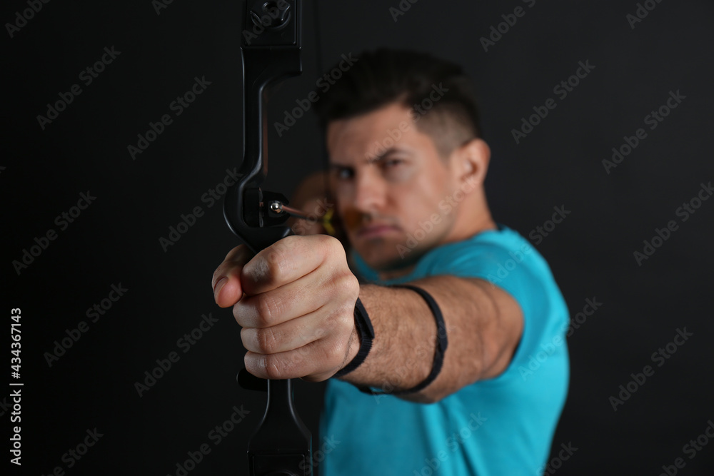 Man with bow and arrow practicing archery against black background, focus on hand Man with bow and arrow practicing archery against black background, focus on hand