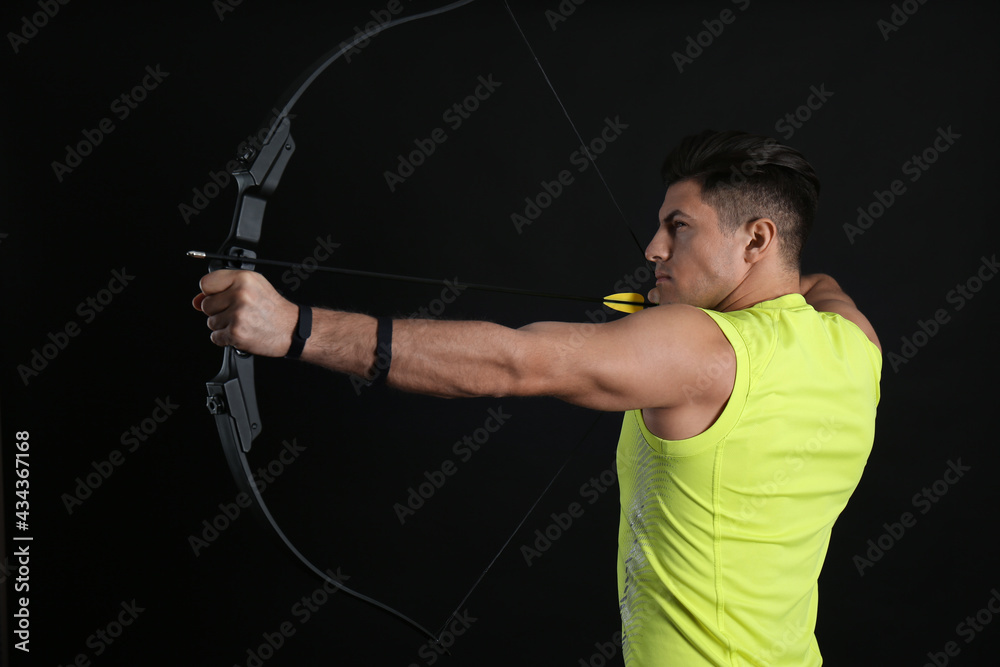 Man with bow and arrow practicing archery on black background Man with bow and arrow practicing archery on black background