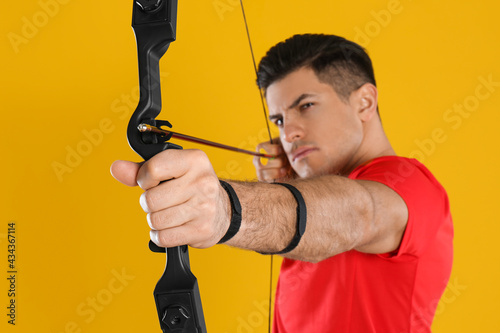 Man with bow and arrow practicing archery against yellow background, focus on hand
