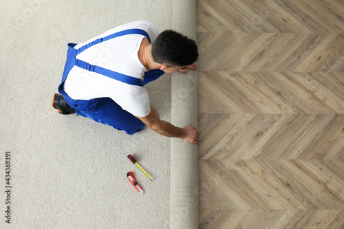 Worker rolling out new carpet indoors, above view