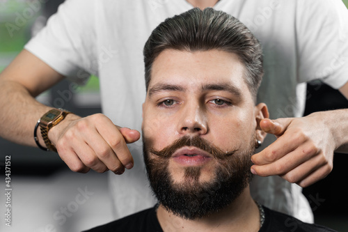 Fixing the shape of mustache with wax. The result of a haircut in a barbershop.