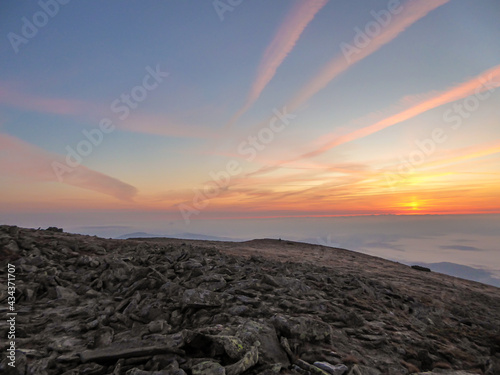 A panoramic view on sun rising above the horizon from the top of Babia Gora in Poland. Thick clouds below. The sky is pink and orange. A few small peaks popping out from the clouds. Freedom. Daybreak