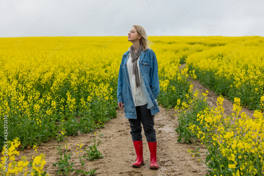 Beautiful blonde in denim jacket and wellington boot on yellow rapeseed field