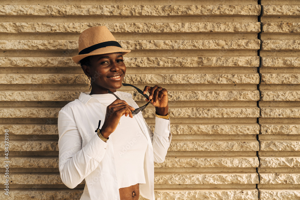 Close-up of an attractive black girl with short hair. She is smiling at the camera and shows a fresh look.Holding sunglasses with hands. Straw hat on her head. Close-up of an attractive black girl with short hair. She is smiling at the camera and shows a fresh look.Holding sunglasses with hands. Straw hat on her head.