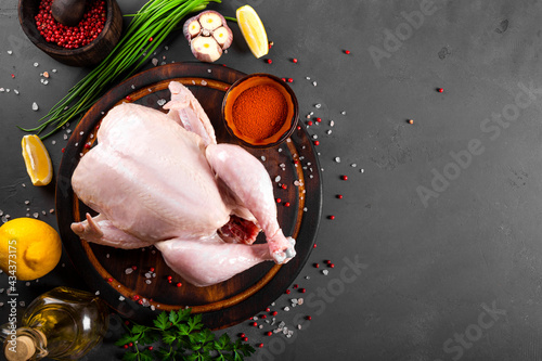 Whole raw chicken on the wooden cutting board and seasonings for cooking it top view, free space for text. Dark gray background