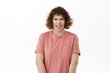 Disgusting. Young woman shows tongue and cringe from dislike, disgusted by something awful, stare aversion, standing in t-shirt against white background