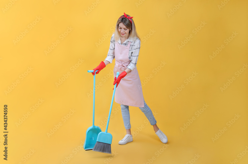 Young housewife with broom and dustpan on yellow background Young housewife with broom and dustpan on yellow background