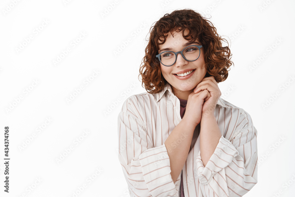 Tender and romantic young girl daydreaming, imaging something beautiful and nice while looking away and smiling, wearing glasses, standing against white background Tender and romantic young girl daydreaming, imaging something beautiful and nice while looking away and smiling, wearing glasses, standing against white background
