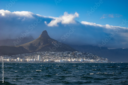 approaching cape town from sea with characteristic Lion`s Head mountain and the spectaclar Table Cloth cloud roller falling down fro Table Mountain in stormy weather