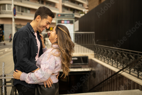 A couple in a romantic moment smiling and looking to each other front of a subway station