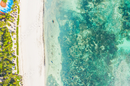 Aerial view of umbrellas, palms on the sandy beach of Indian Ocean at sunset. Summer in Zanzibar, Africa. Tropical landscape with palm trees, parasols, walking people, blue water, waves. Top view