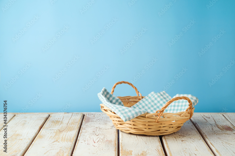 Empty wicker basket with tablecloth on rustic table over blue wall  background.  Kitchen mock up for design and product display. - obrazy, fototapety, plakaty 