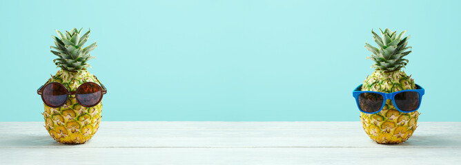 Summer holidays vacation and beach party concept. Pineapple with sunglasses on wooden table over blue background.