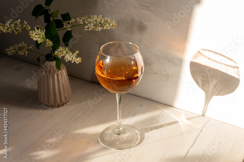 glass of rose wine in sun light, shadow, bird cherry flowers in vase on white backgroun