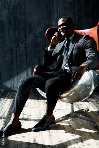 Stylish african american manager sitting on a chair in the center of the room and talking on the phone laughing © DmitryStock