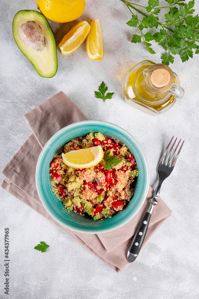  Salmon salad with tomatoes, avocado and quinoa in a blue bowl on a light gray table top view, a dish of balanced nutrition. Vertical photo
