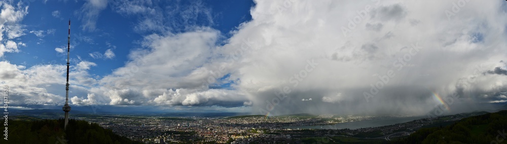 Panorama shot from Uetliberg on Zurich with cloudy skies and green forests with a beautiful rainbow 