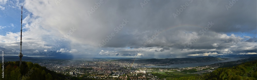 Panorama shot from Uetliberg on Zurich with cloudy skies and green forests with a beautiful rainbow 