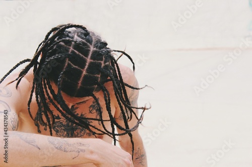 Portrait of young man shirtless with tattoos on skin and tight hair braids , hairstyle / style 