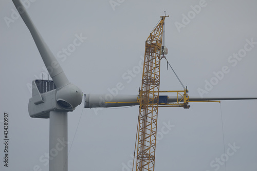 A crawler crane is hoisting a rotor blade of a new wind turbine