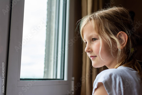 Sad child looking out the window on rainy day. little girl in pajamas looking out the window. upset unhappy child waiting for parents, thinking about problems, 