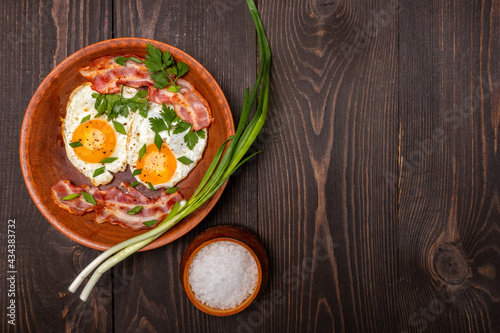fried eggs with bacon and herbs on a wooden background top view