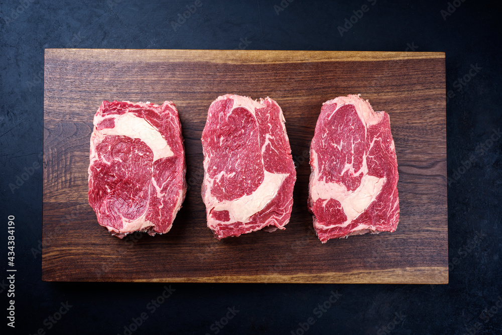 Modern style raw dry aged wagyu rib-eye beef steaks offered as top view on a wooden design board with copy space