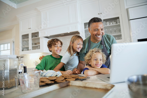 Happy family using laptop while cookies cool on kitchen counter