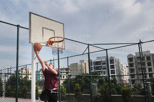 Basketball player throws basketball to a hoop. Young adult man plays basketball at outdoor court. Basketball game at public sports court © Philipp Berezhnoy