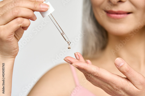 Fotografía Closeup cut portrait of senior mature older Asian woman putting drop of antiaging pipette serum essence oil on finger hand