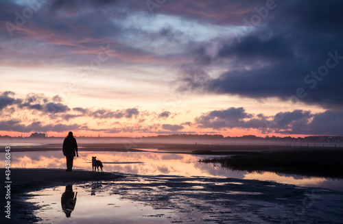 Silhouette of the woman with her dog enjoy the scenic sunset view over sandy beach and misty coast toward city lights in the distance