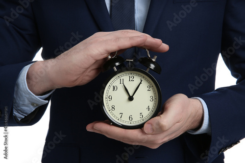 Businessman holding alarm clock, closeup view. Time management