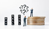 Black cubes with BUY, SELL and HODL text on white background. Thinking businessman figurine with question marks above his head looking at cubes while other one standing on stack.
