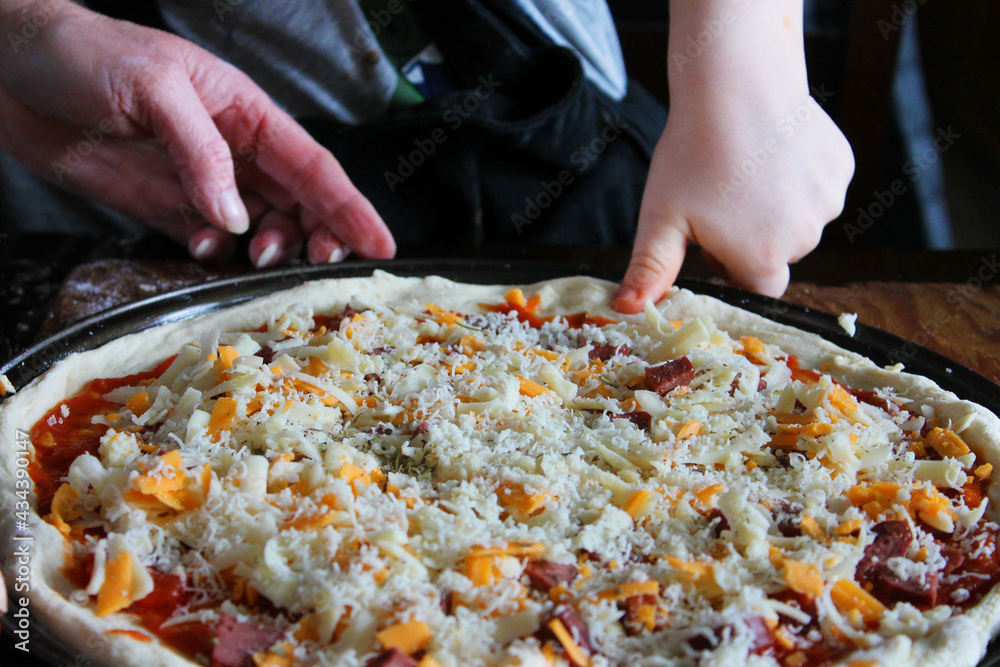 Close-up of woman and small child making homemade pizza. Hands only in frame.