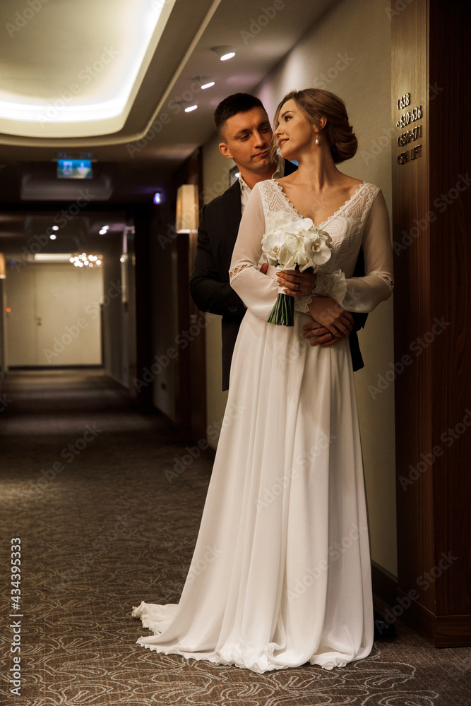 Romantic meeting of the bride and groom in the hotel corridor. The groom gives the bride a wedding bouquet of white roses. Morning before the wedding. Romantic meeting of the bride and groom in the hotel corridor. The groom gives the bride a wedding bouquet of white roses. Morning before the wedding.