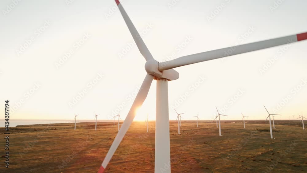 Large wind turbines with blades in field aerial view bright orange sunset blue sky wind park slow motion drone slide back. Silhouettes windmills orange sun disc summer lens flare. Alternative energy Large wind turbines with blades in field aerial view bright orange sunset blue sky wind park slow motion drone slide back. Silhouettes windmills orange sun disc summer lens flare. Alternative energy
