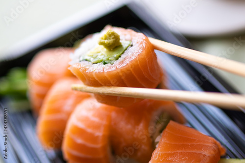 Chopsticks with philadelphia sushi roll with fresh salmon, avocado and wasabi in closeup macro shot