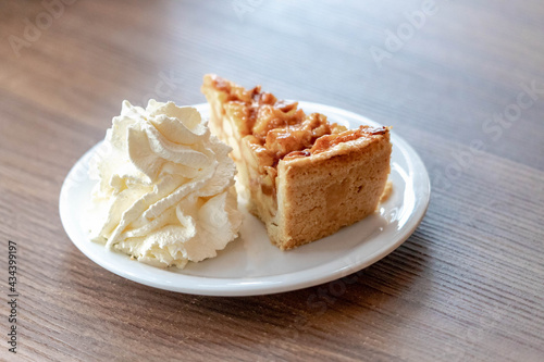 A piece of apple pie on white plate served with whipping cream on the side, Homemade apple pie on wooden table, Freshly baked.