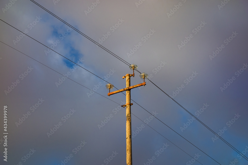 Very old electricity pylon with wires, cables against cloudy sky Very old electricity pylon with wires, cables against cloudy sky