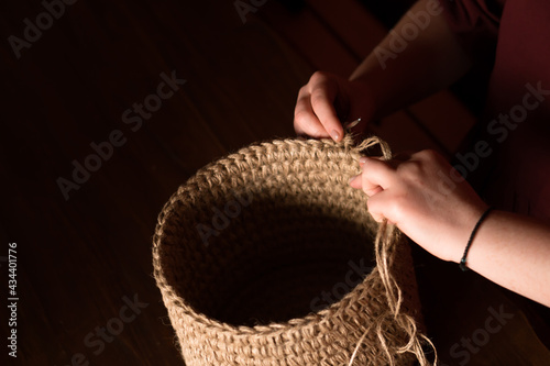 hands of woman crocheting decorative interior backet from jute photo