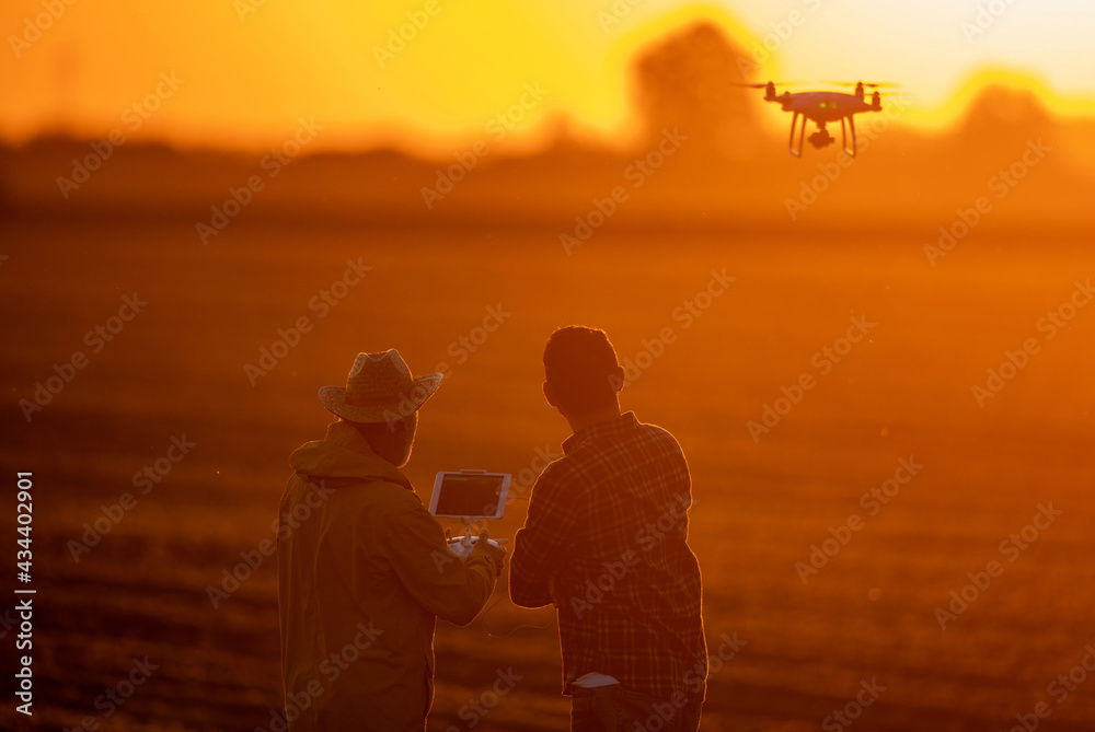 Fototapeta premium Two farmers using drone surveying field at sunset