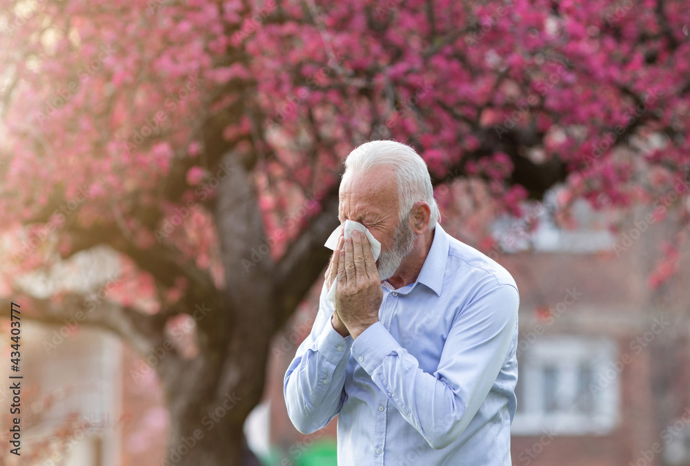 Man with allergy symptoms sneezing outside in springtime - obrazy, fototapety, plakaty 