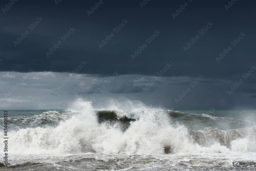 View of a stormy sea and dark cloudy dramatic sky, big waves are crashing on the shore