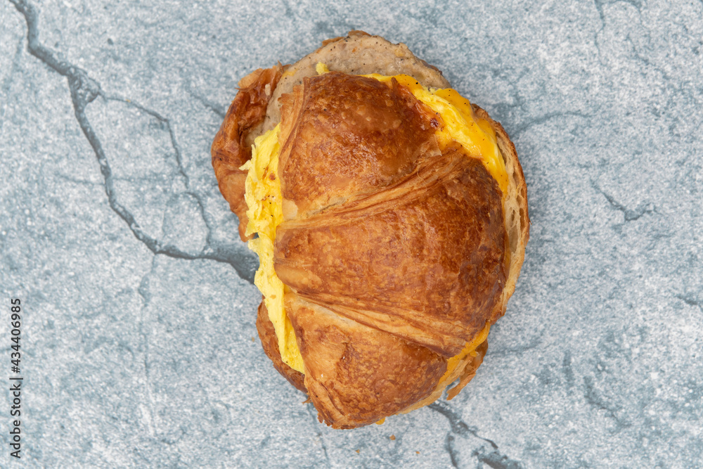 Overhead view of delicious croissant sandwich loaded with scrambled eggs, melted cheese, and sausage patty for a complete meal. Overhead view of delicious croissant sandwich loaded with scrambled eggs, melted cheese, and sausage patty for a complete meal.