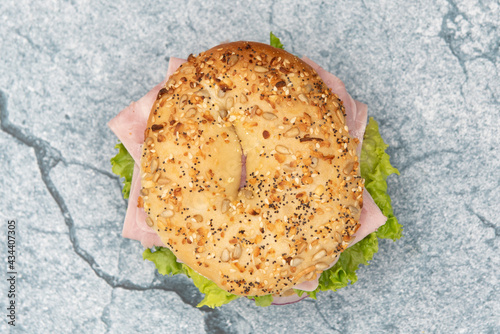 Overhead view of everything bagel bun envelops this non traditional ham sandwich loaded with lettuce, meat slices, and onion. photo