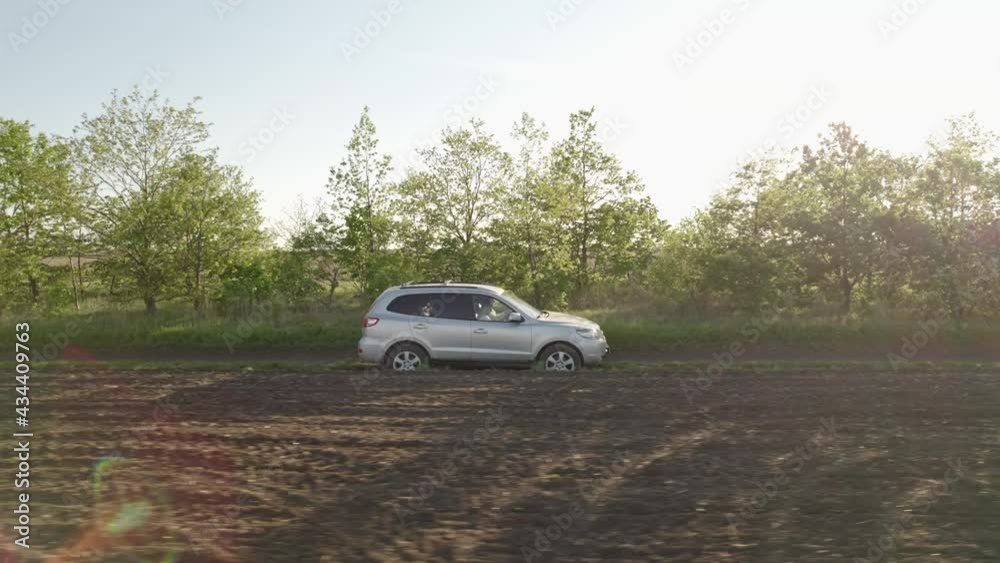 Car drives along rural road kicking up dust among green wheat field aerial view blue sky at sunset in spring. Wind park agricultural farm. Alternative energy eco nature concept Car drives along rural road kicking up dust among green wheat field aerial view blue sky at sunset in spring. Wind park agricultural farm. Alternative energy eco nature concept