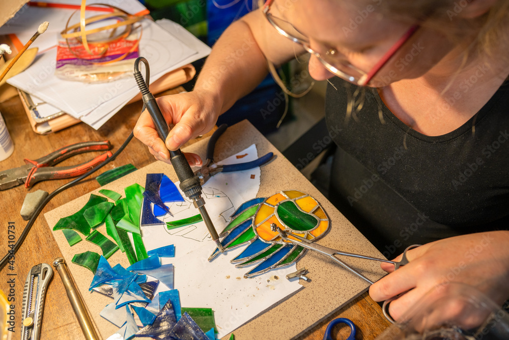 soldering the stained glass window, woman is making a stained glass