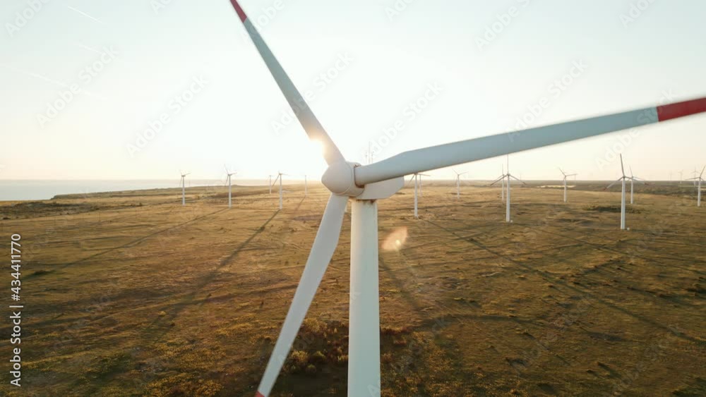 Large wind turbines with blades in field aerial view bright orange sunset blue sky wind park slow motion drone slide back. Silhouettes windmills orange sun disc summer lens flare. Alternative energy Large wind turbines with blades in field aerial view bright orange sunset blue sky wind park slow motion drone slide back. Silhouettes windmills orange sun disc summer lens flare. Alternative energy